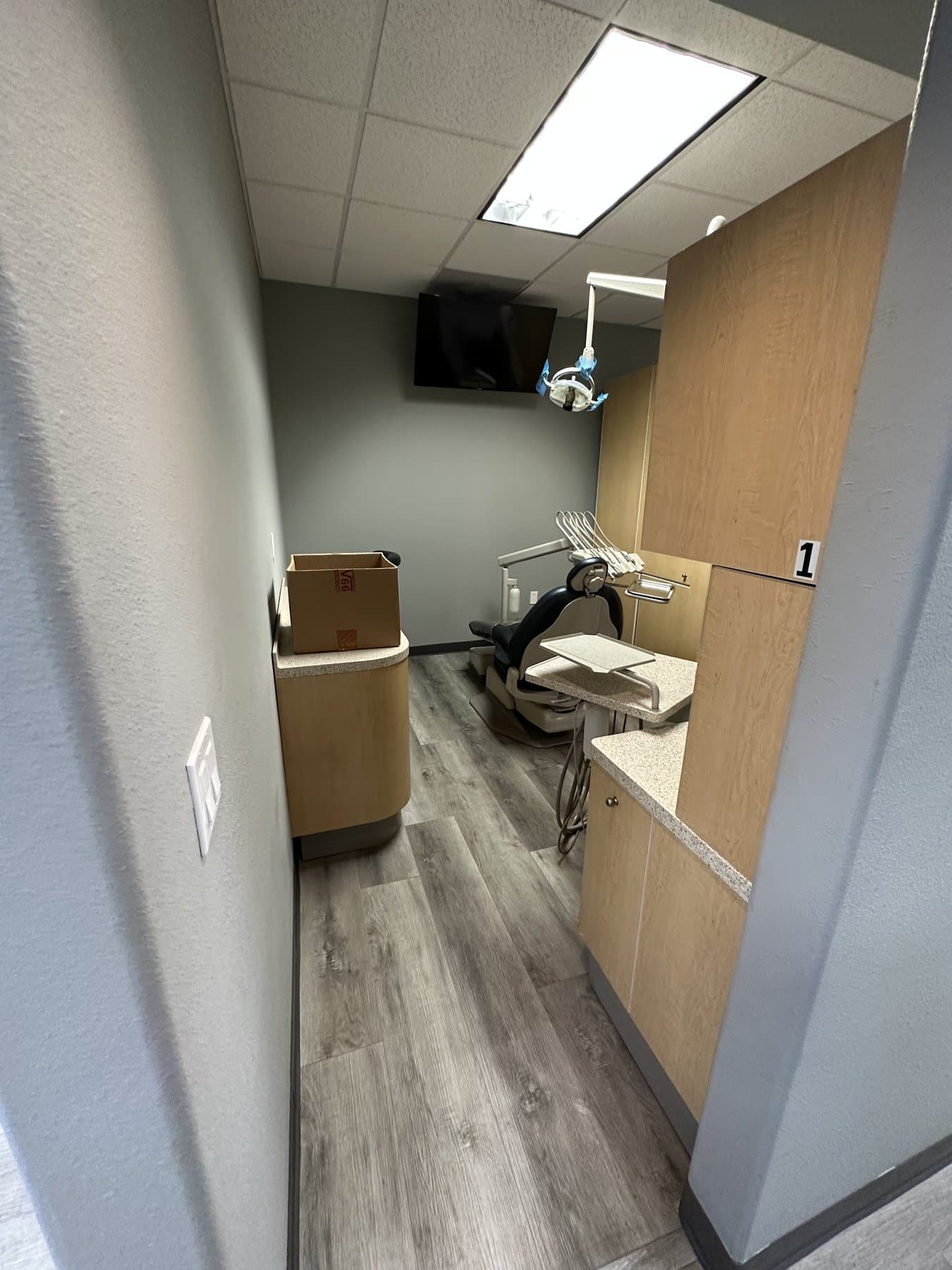 Dental operatory with a treatment chair, overhead light, delivery unit, and a monitor facing the chair.